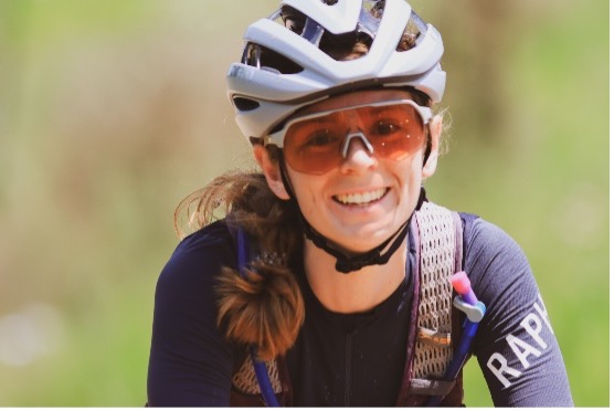 Person cycling outdoors with helmet, sunglasses, jersey; blurred background shows movement.