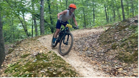 Mountain biker in orange helmet on forest dirt trail