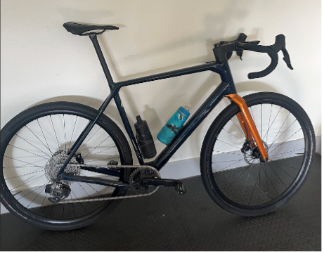 Road bicycle with dark frame, drop handlebars, orange fork, and two bottle holders and bottles.