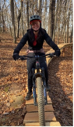 Mountain biker with helmet on wooden trail in a leafy forest setting.