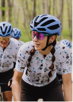 Cyclists with matching jerseys and blue helmets ride through a wooded area.