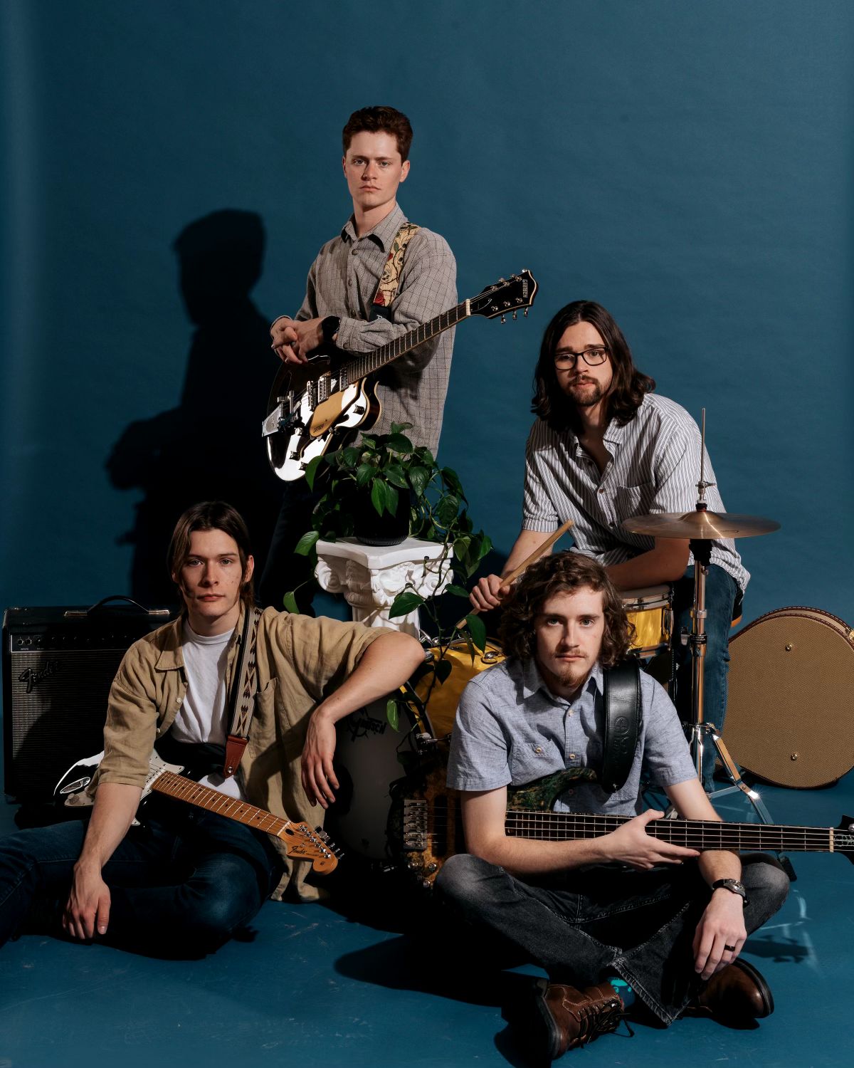 Four men with guitars and drums posing against a blue background.