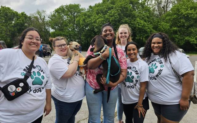 Women holding dogs and wearing matching t-shirts outside.