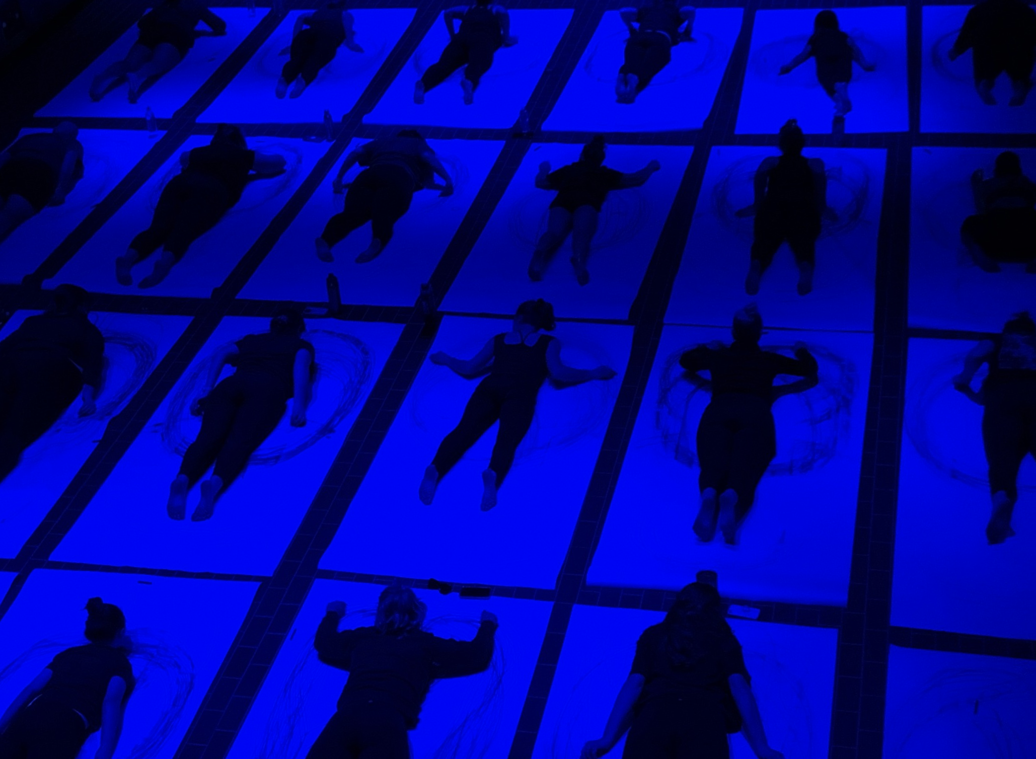 People lying on large paper sheets in rows, illuminated by blue light.
