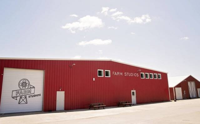 Red barn-style building labeled Farm Studios with doors and windows, on paved surface, clear sky.