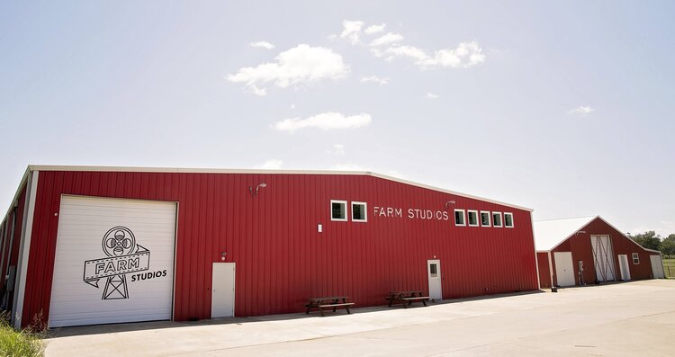 Red barn-style building labeled Farm Studios with doors and windows, on paved surface, clear sky.