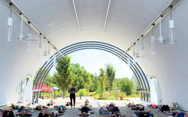 People in a yoga session under an open arch canopy, surrounded by greenery and natural light.
