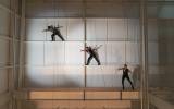 Performers suspended on wall with harnesses in well-lit indoor space, creating dynamic poses.