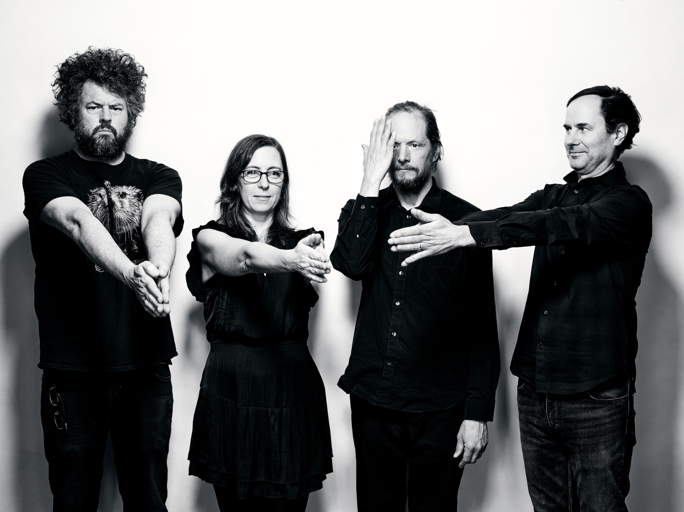 Unwound Four individuals in dark clothing pose with varied hand gestures against a white background.