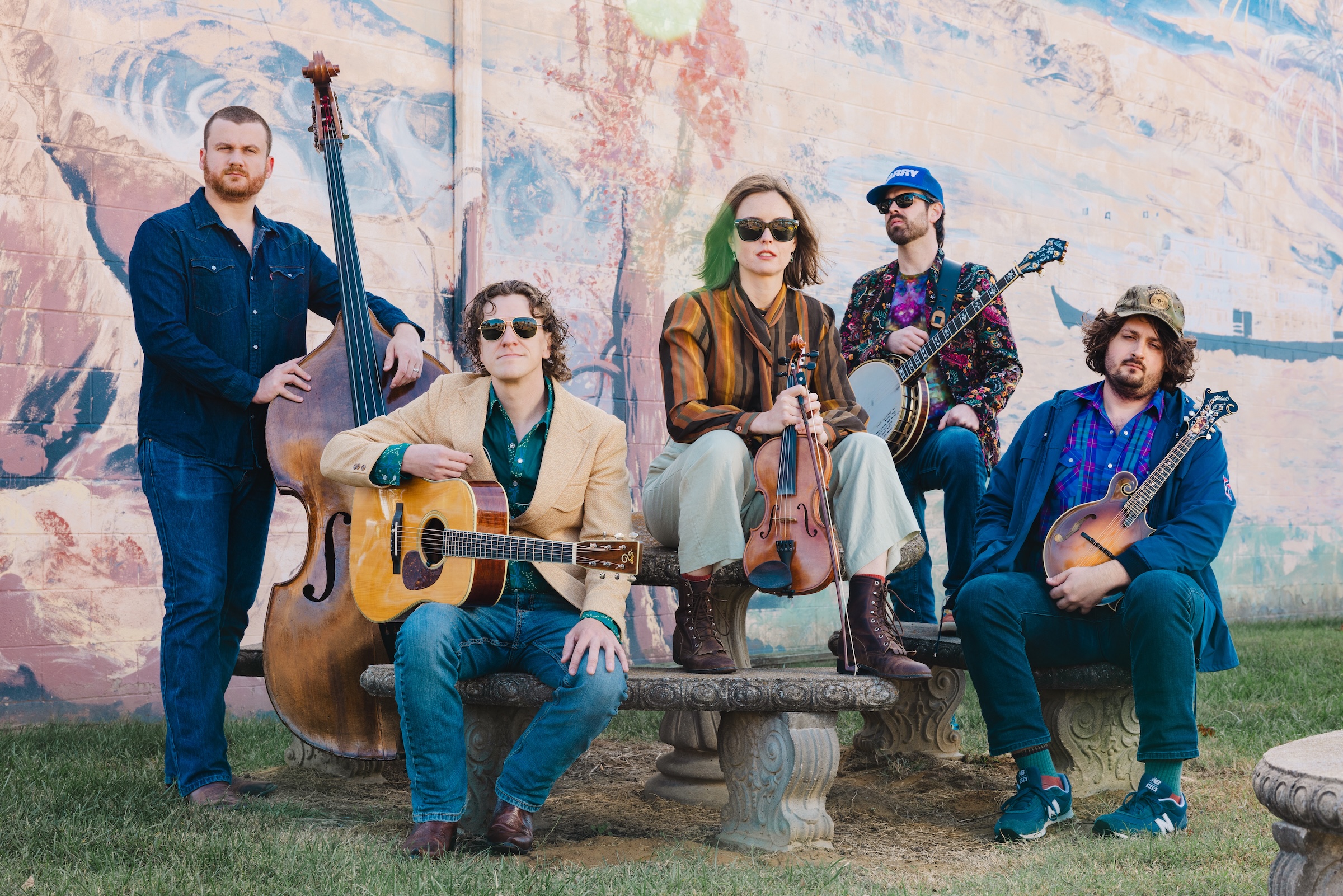 East Nash Grass Group of five with instruments outdoors against a colorful mural, suggesting a music event.