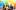 Photo by Ironside Photography / Stephen Ironside. Four people embrace under a rainbow balloon arch with trees and urban background.