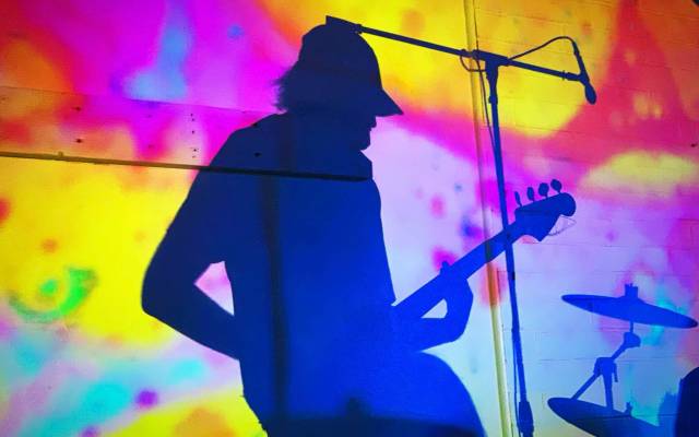 Silhouette of guitarist and drum set on colorful background with microphone.