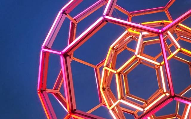Neon-lit geometric sculpture of interconnected hexagons and pentagons against a dark sky