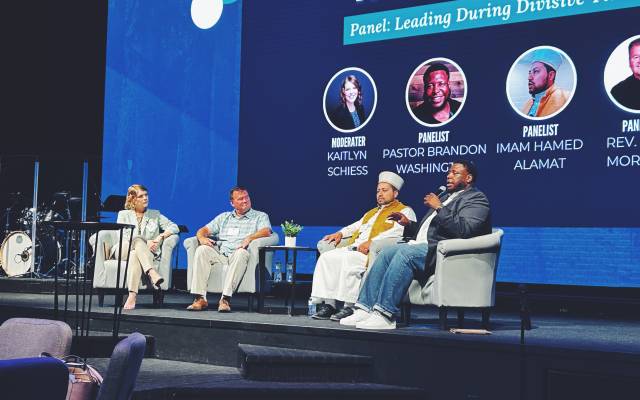 Panel discussion on Leading During Divisive Times with four speakers seated on stage.