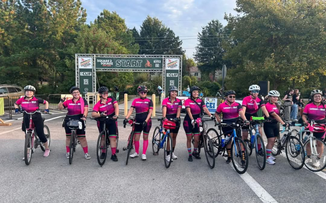 Cycling team in matching pink and black gear lined up with bikes at Square 2 Square race start.