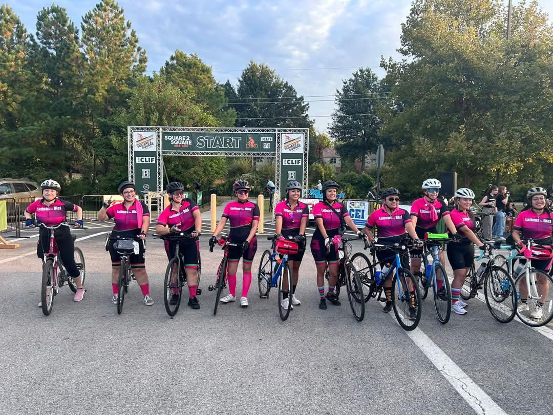 Cycling team in matching pink and black gear lined up with bikes at Square 2 Square race start.