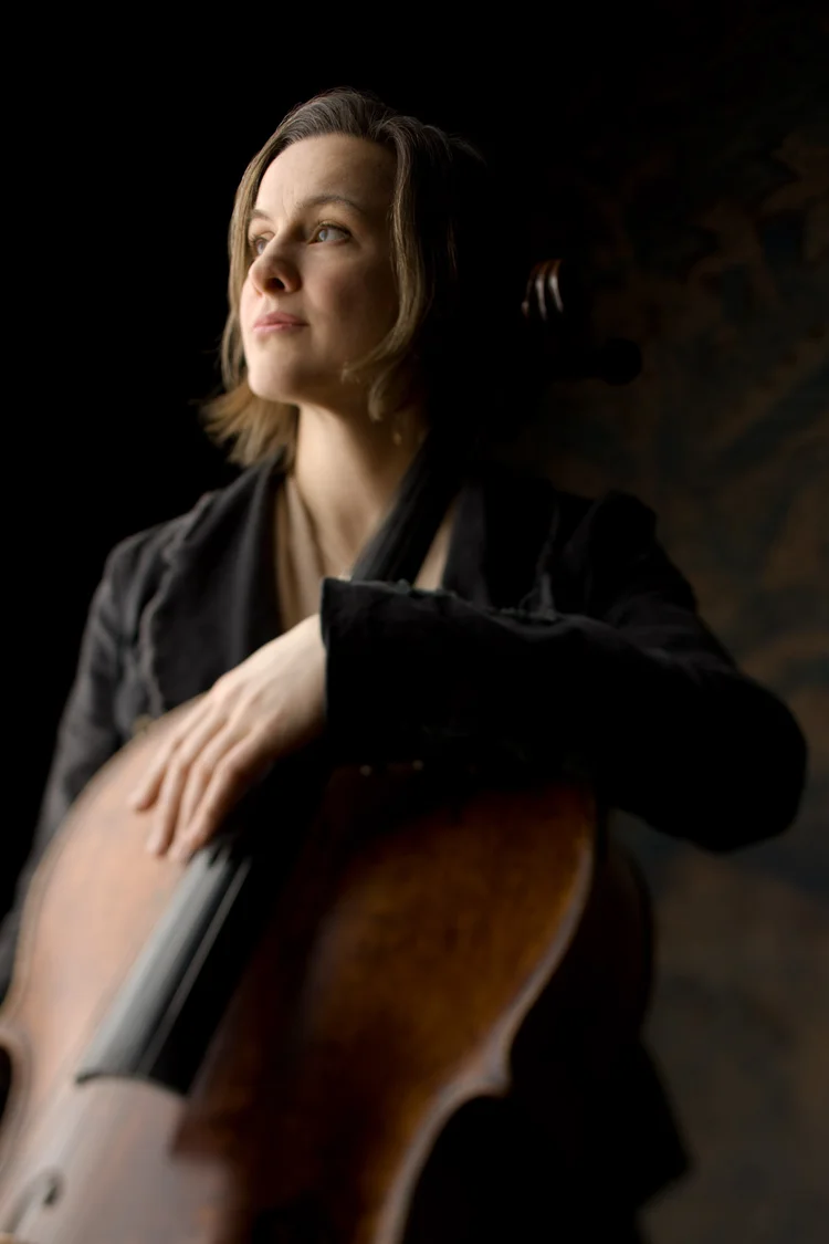 Kantinka-Kleijin-photo-2 Woman holding a cello with soft light on her face and instrument against a dark background