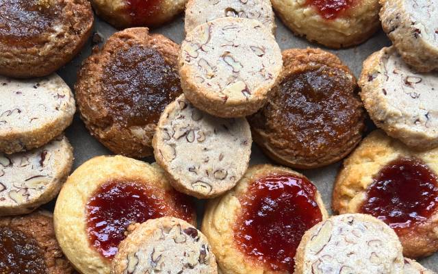 Assorted cookies with nut pieces and jam-filled centers arranged on a flat surface