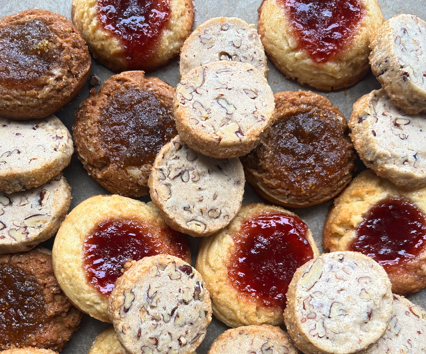 Assorted cookies with nut pieces and jam-filled centers arranged on a flat surface