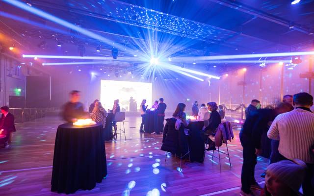 Indoor event space with groups socializing under colorful lights and a disco ball projection.