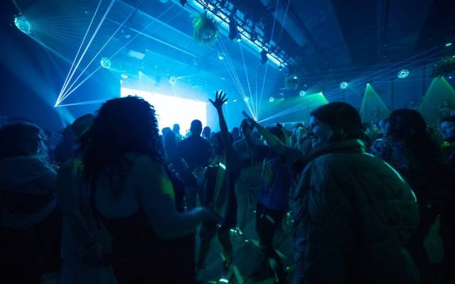 Crowd dancing in a dimly lit venue with blue and green laser lights and raised hands.