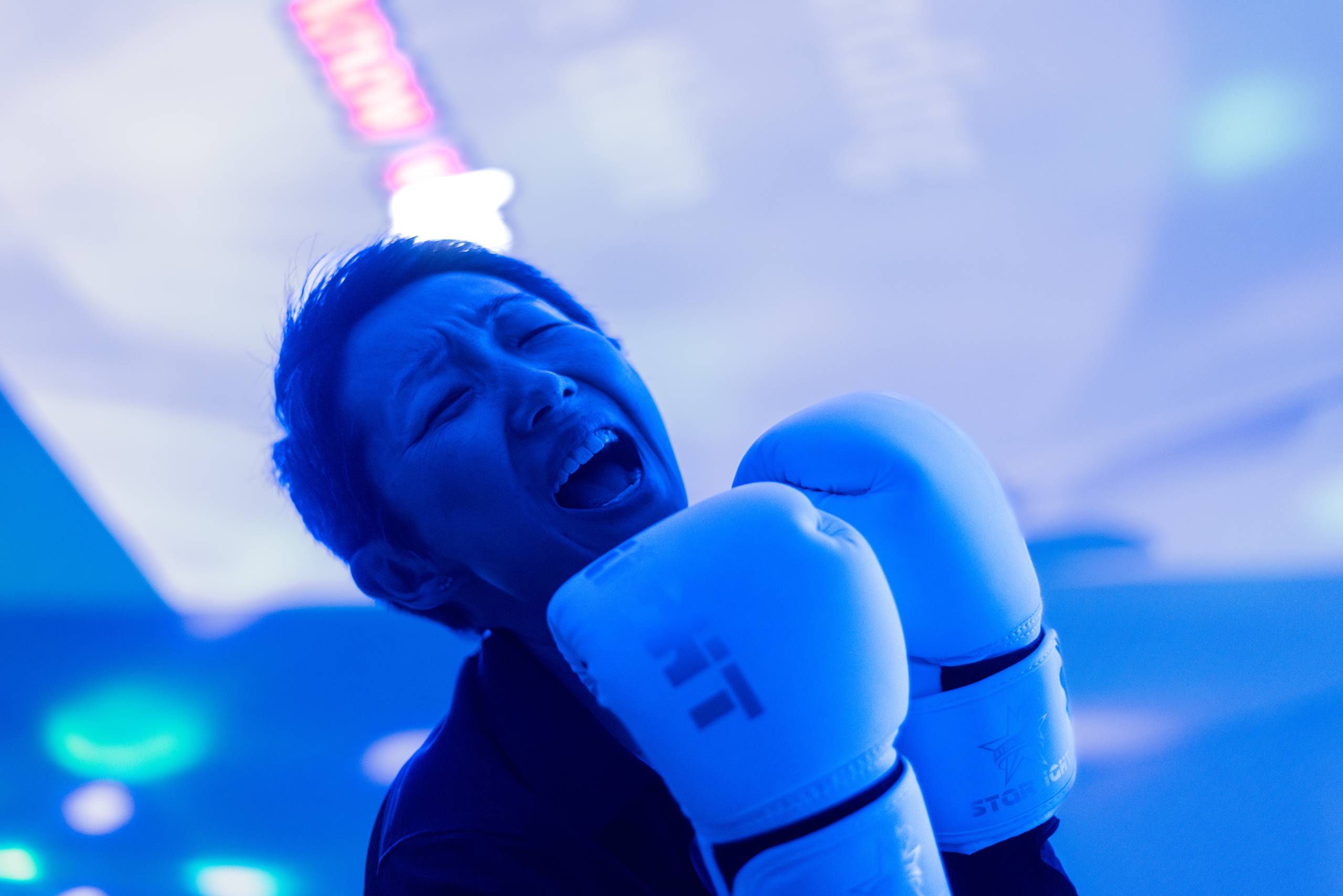 Person with white boxing gloves shouting under blue lighting in a close-up shot