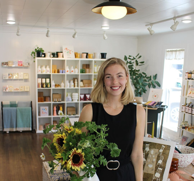Woman in black dress holding vase with sunflowers inside a bright store with shelves and displays.
