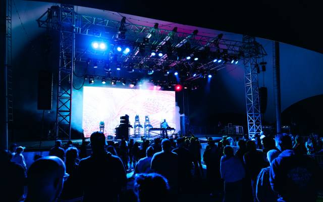 Outdoor nighttime concert with a DJ performing on stage and an audience watching.
