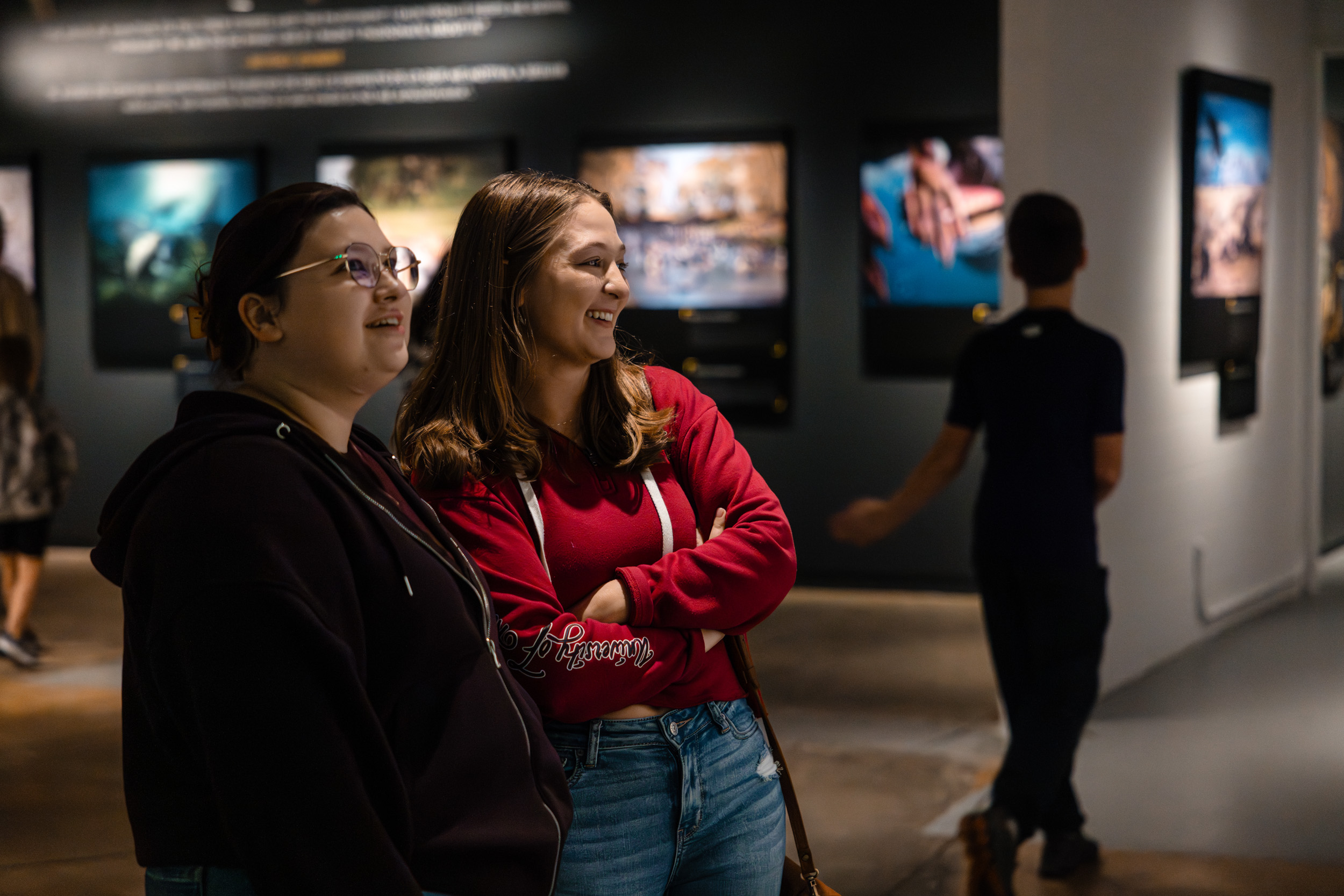 Two women stand smiling in an art gallery with photographs on the walls behind them.