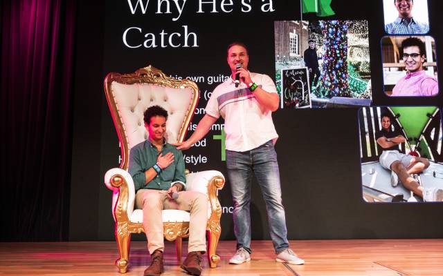 Two men on a stage, one seated in an ornate chair, the other speaking into a microphone.
