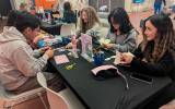 Teenagers seated at a table cutting paper and crafting in a community event space.
