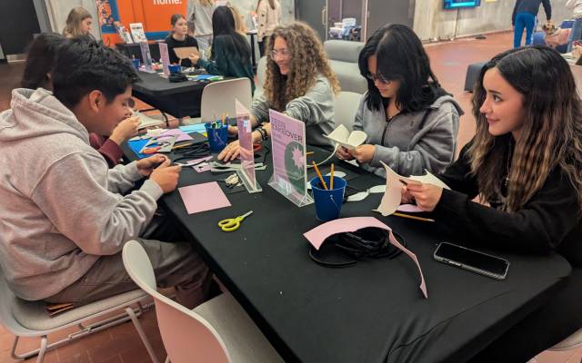 Teenagers seated at a table cutting paper and crafting in a community event space.
