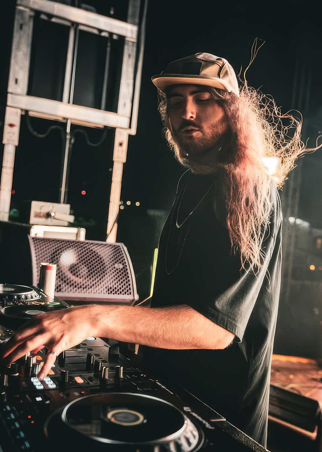 Person wearing a cap operating DJ equipment with long hair and abstract light trails in background