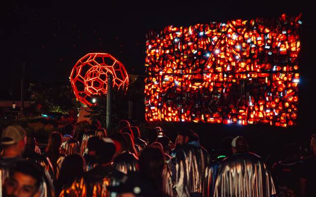 Crowd wearing silver capes viewing illuminated red geometric and rectangular light art installations at night.