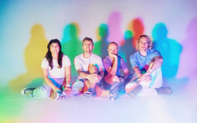 Four people sit on the floor with colorful shadows cast on a white background.