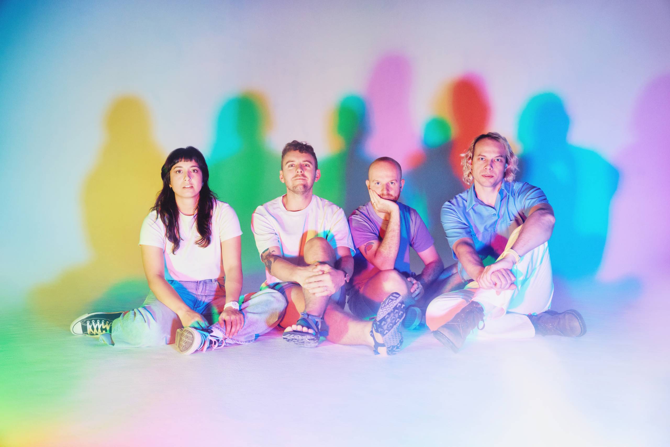 Four people sit on the floor with colorful shadows cast on a white background.