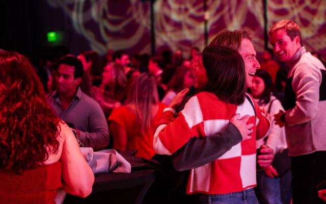 People socializing and hugging in a dimly lit room with red lighting and patterned walls.