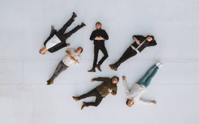 Six people lying on a light surface in a star formation with heads near the center.