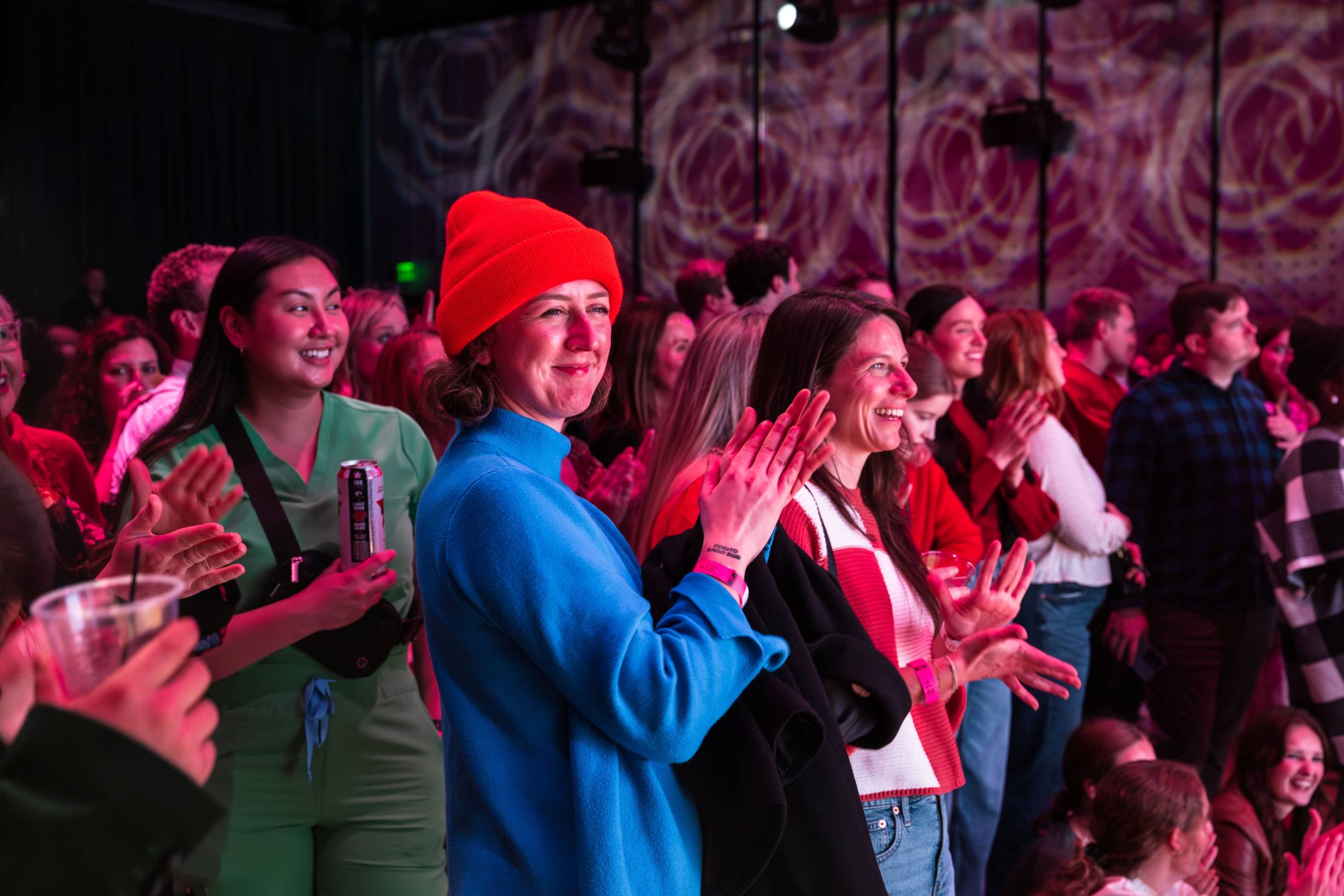 Group of people indoors clapping and smiling under red lighting with patterned walls.