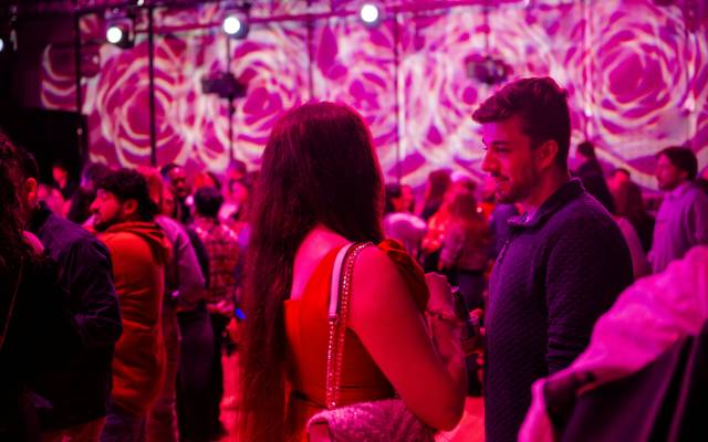 Indoor social event with people under pink and purple lighting and swirling wall projections