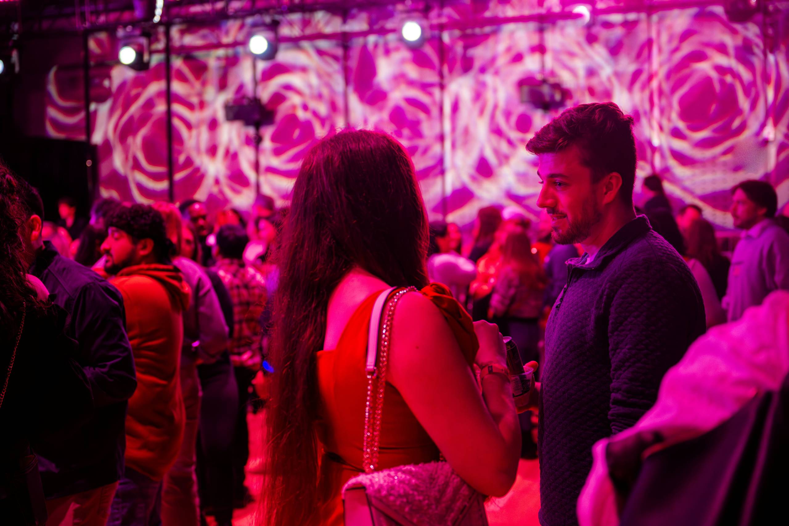 Indoor social event with people under pink and purple lighting and swirling wall projections