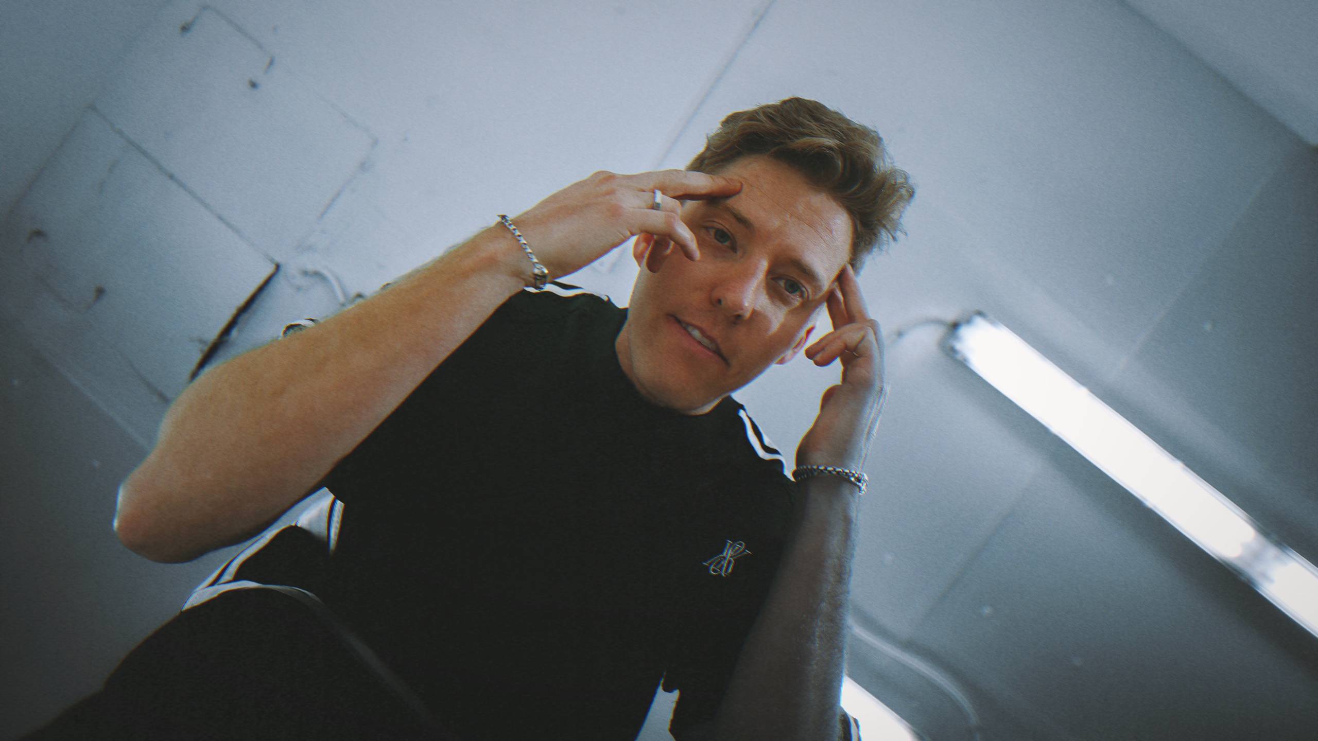 Young man in black shirt indoors, touching temples with hands, reflective expression.