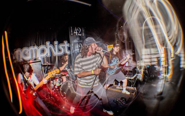 Live band performing on stage with singer, guitarist, and drummer, with light trails.