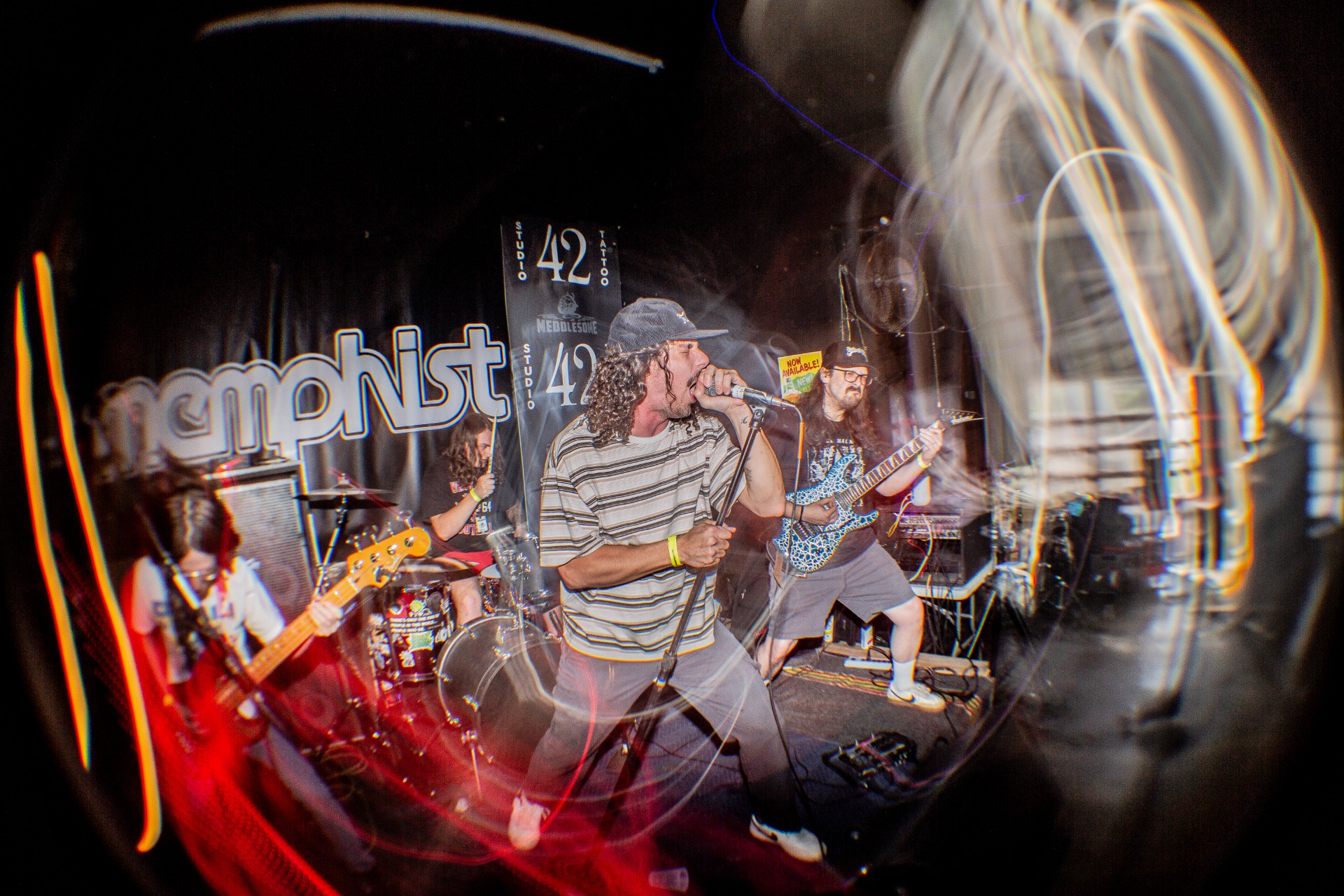 Live band performing on stage with singer, guitarist, and drummer, with light trails.