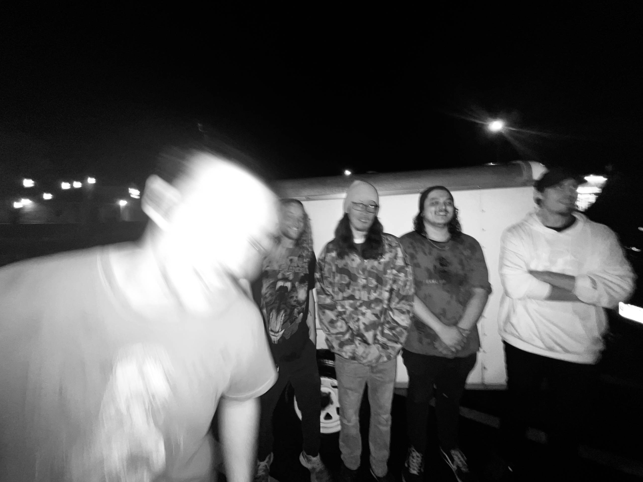 Group of young people smiling outdoors at night, standing together, some faces visible.