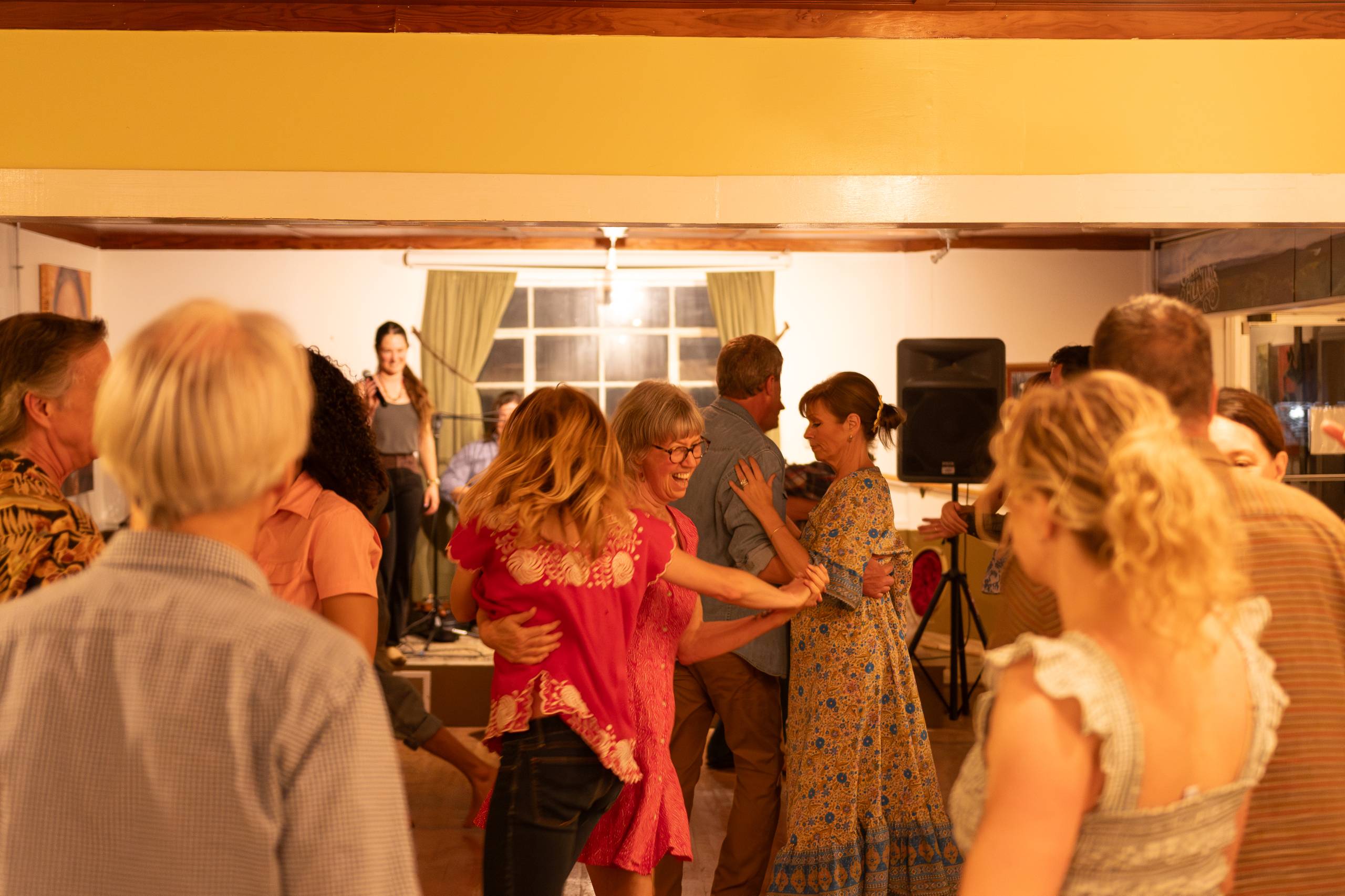 People dancing closely at a lively indoor party with a singer on stage in back.