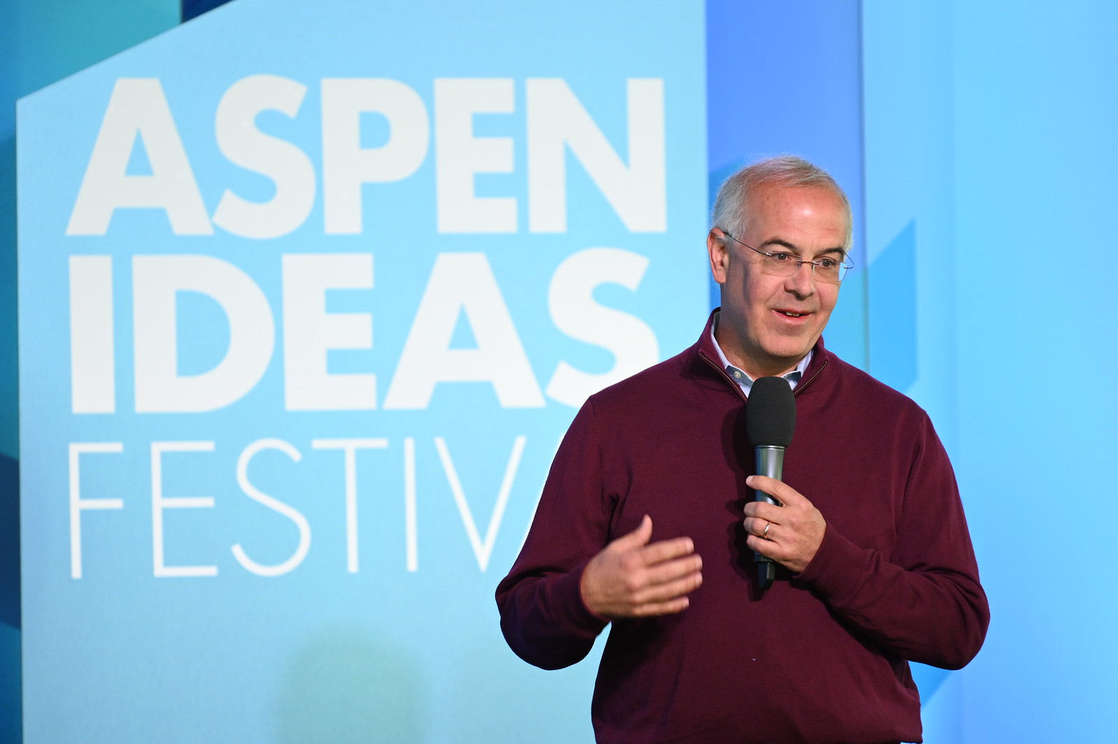 Speaker with microphone on stage at Aspen Ideas Festival, blue backdrop text
