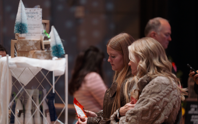 Two young women examine a red and white card at a gift shop counter.