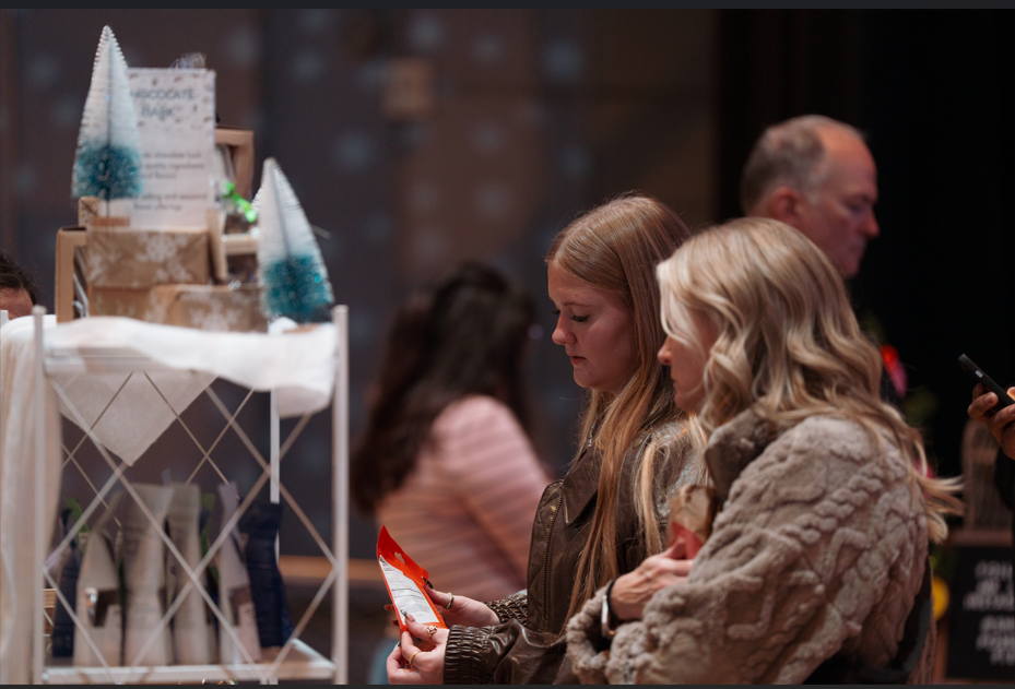 Two young women examine a red and white card at a gift shop counter.