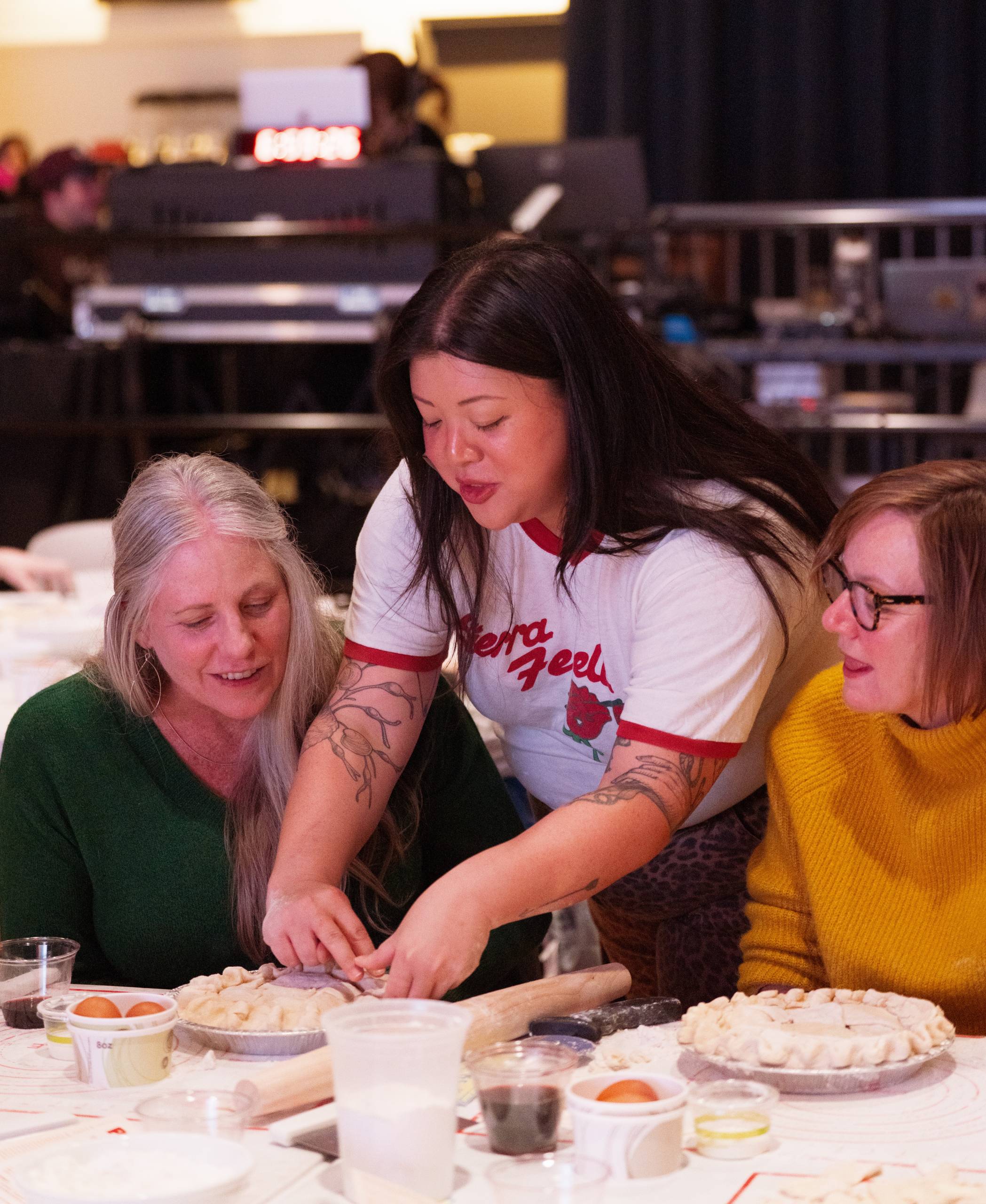 People gathered around a table, rolling dough and shaping pastries in a kitchen.